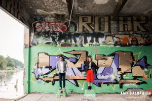 engaged couple standing in front of graffiti backdrop