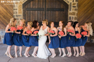 bridesmaids laughing with each other wearing navy dresses with coral bouquets