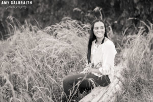 high school senior in black and white image sitting on log at discovery park