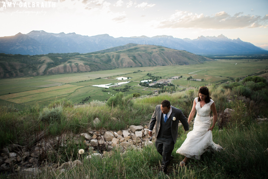 A bride and groom stroll on top of a bluff during their mountain wedding reception in Grand Teton National Park