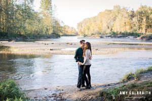 couple standing next to snoqualmie river during engagement session