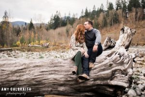 a couple sitting on a large fallen log near the river at stevens pass