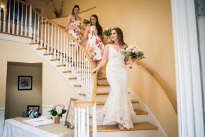 bride and bridesmaids walk down the staircase at tibbetts creek manor
