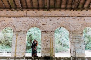 engaged couple kisses in archway of old brick building at manchester state park