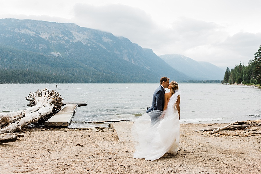 bride and groom kissing next to mountain lake