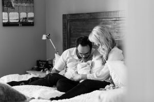 parents snuggling newborn baby in their bedroom during lifestyle newborn session