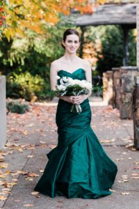 A bride wearing an emerald wedding gown carries an ivory bouquet as she gets ready for her autumn Salish Lodge wedding, photographed by Seattle wedding photographer Amy Galbraith