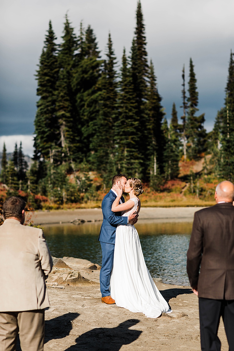 A bride and groom share a first kiss after their hiking elopement near Mt Rainier at a small alpine lake