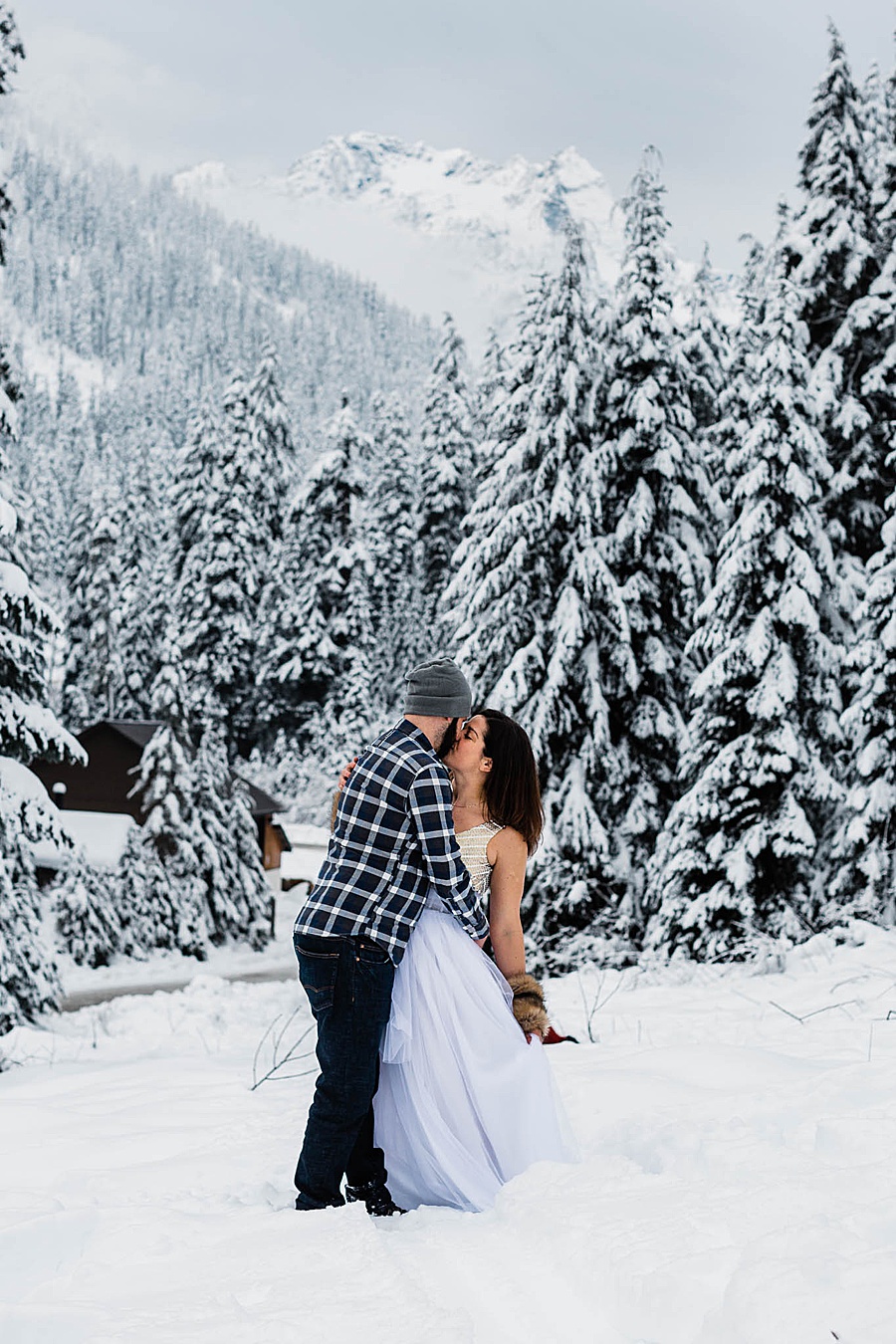 A couple kisses among a snowy winter scene at Snoqualmie Pass in Washington