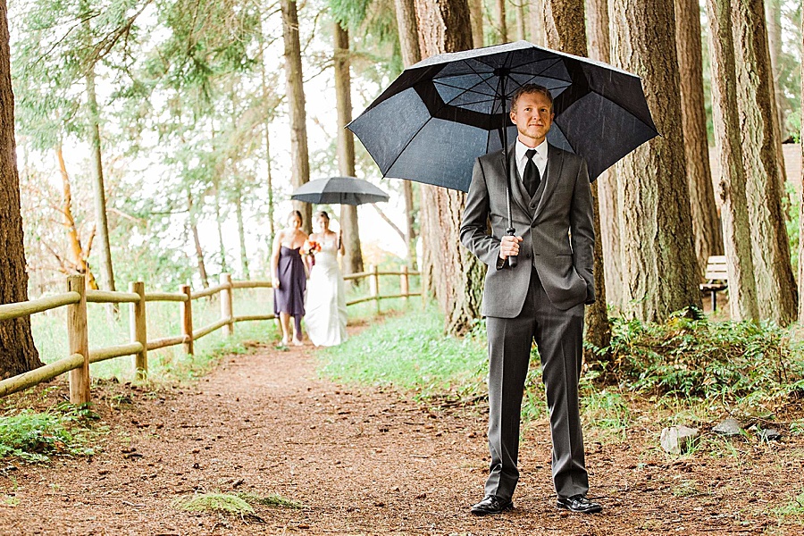 A groom waits for his bride under an umbrella at a wedding at Kitsap Memorial State Park