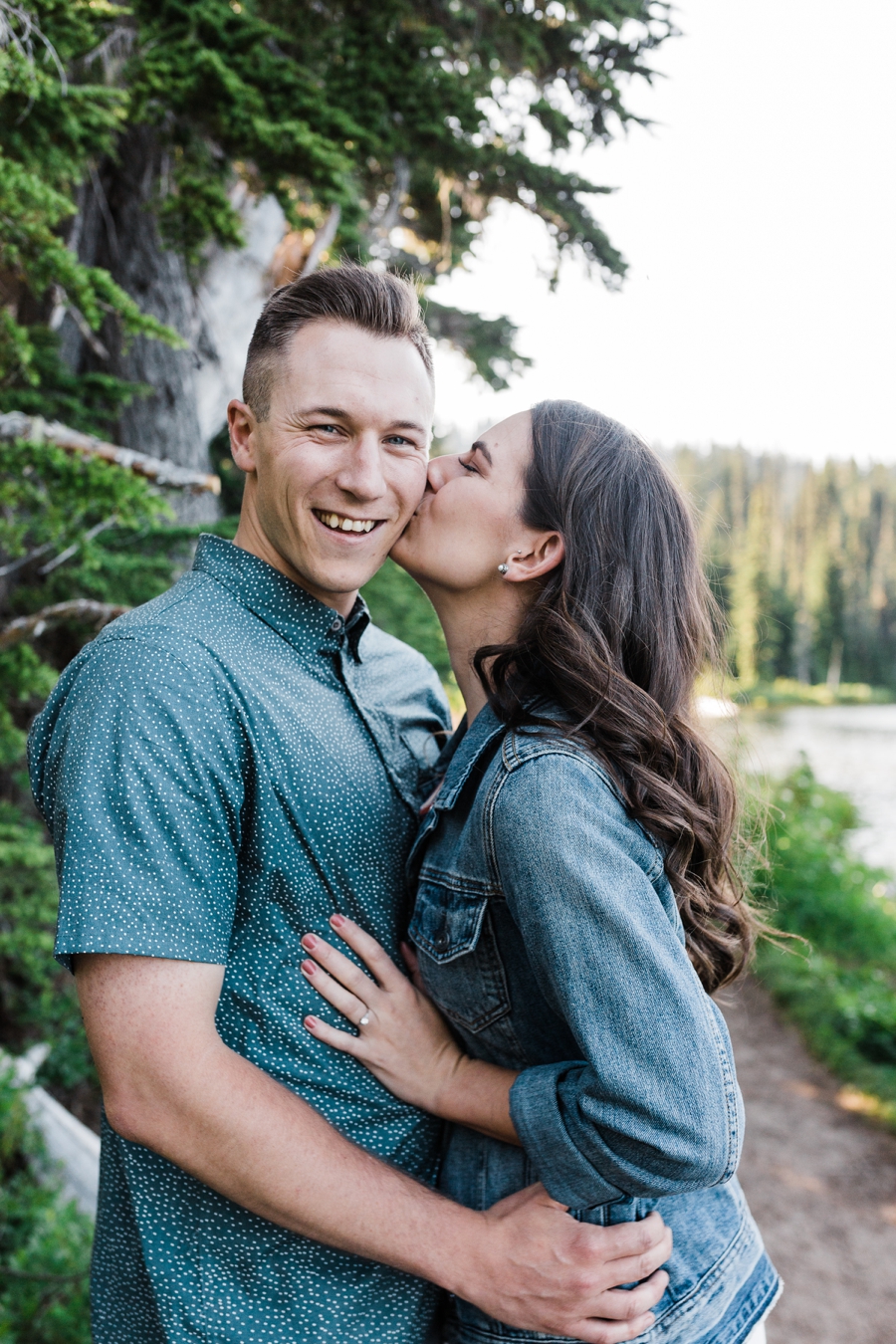 a girl kisses her fiance on the cheek during their engagement session in the mountains