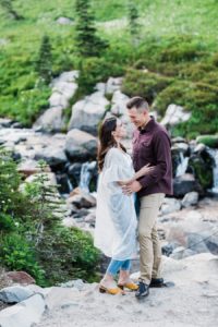 A couple embraces next to a waterfall in the Paradise are of Mt Rainier National Park