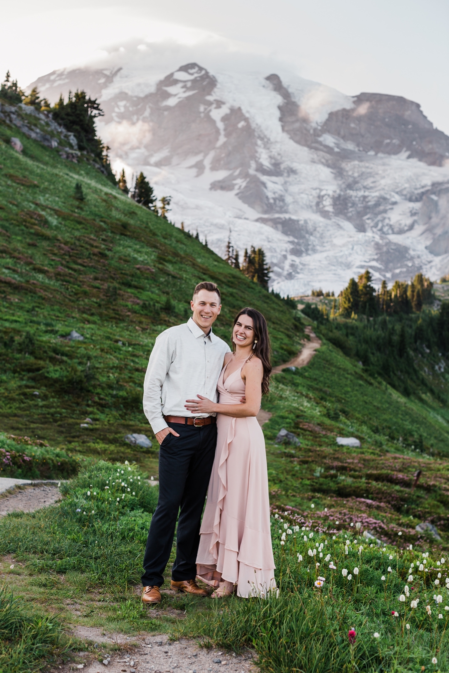 A couple stands together backdropped by stunning Mt Rainier at sunset