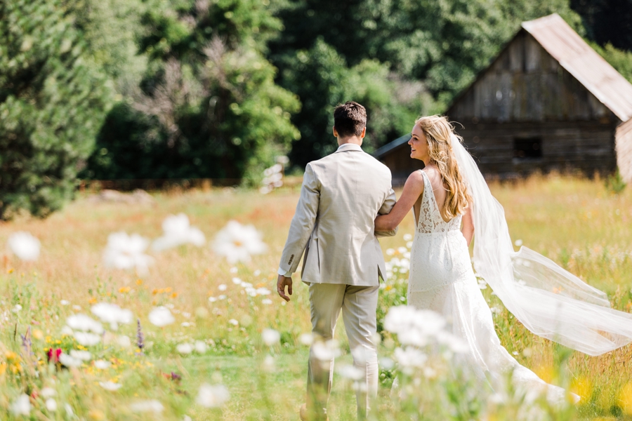 A bride and groom walk through a field of wildflowers at a venue in Leavenworth, Washington by Seattle mountain wedding photographer Amy Galbraith