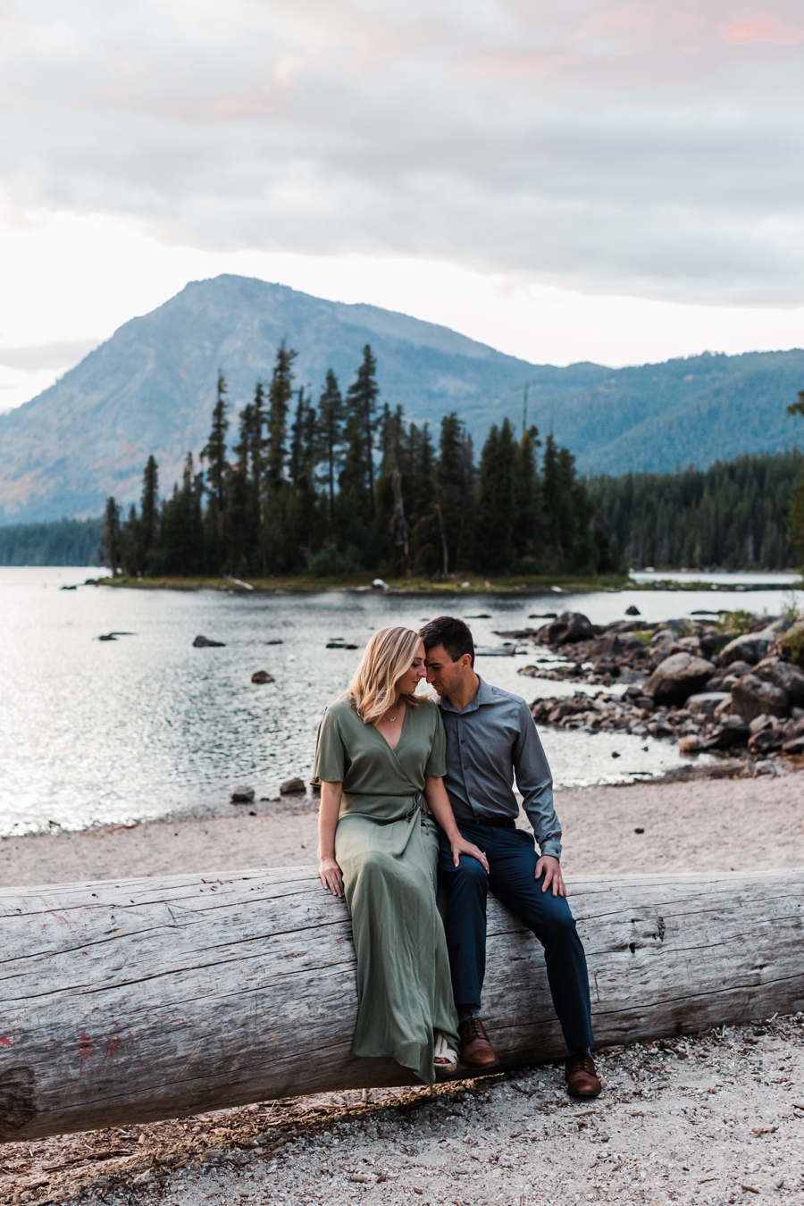 A couple snuggles together on a large fallen log at Lake Wenatchee during their mountain engagement photos at dusk at Lake Wenatchee by mountain wedding photographer Amy Galbraith