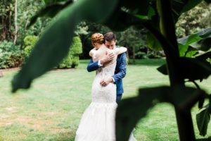 A groom embraces his bride under a banana plant at Maronis Meadows in Snohomish by Seattle wedding photographer Amy Galbraith