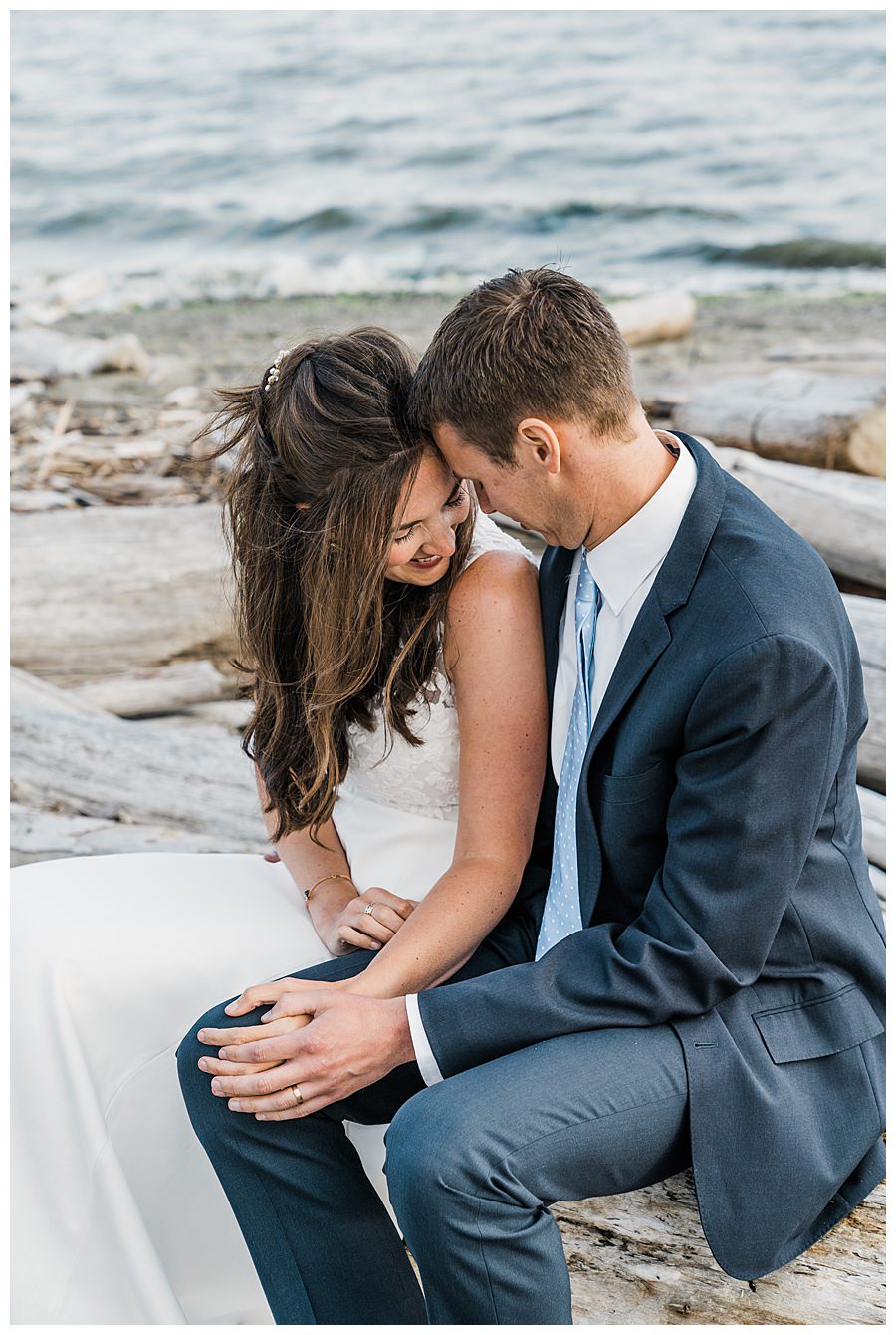 A bride and groom snuggle together on the beach during their Camano Island elopement photographed by Amy Galbraith