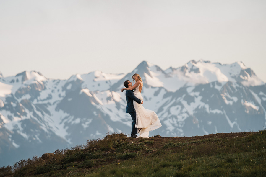 A groom lifts his bride in front of a breathtaking mountain landscape on Hurricane Ridge in Olympic National Park