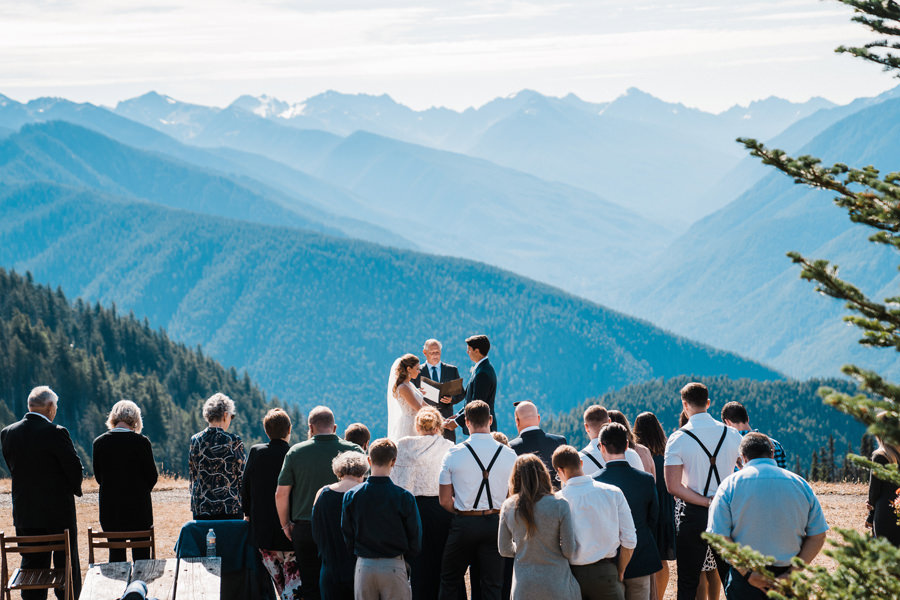 A couple says their vows surrounded by a small group of guests on Hurricane Ridge in Olympic National Park as mountains tower high behind them