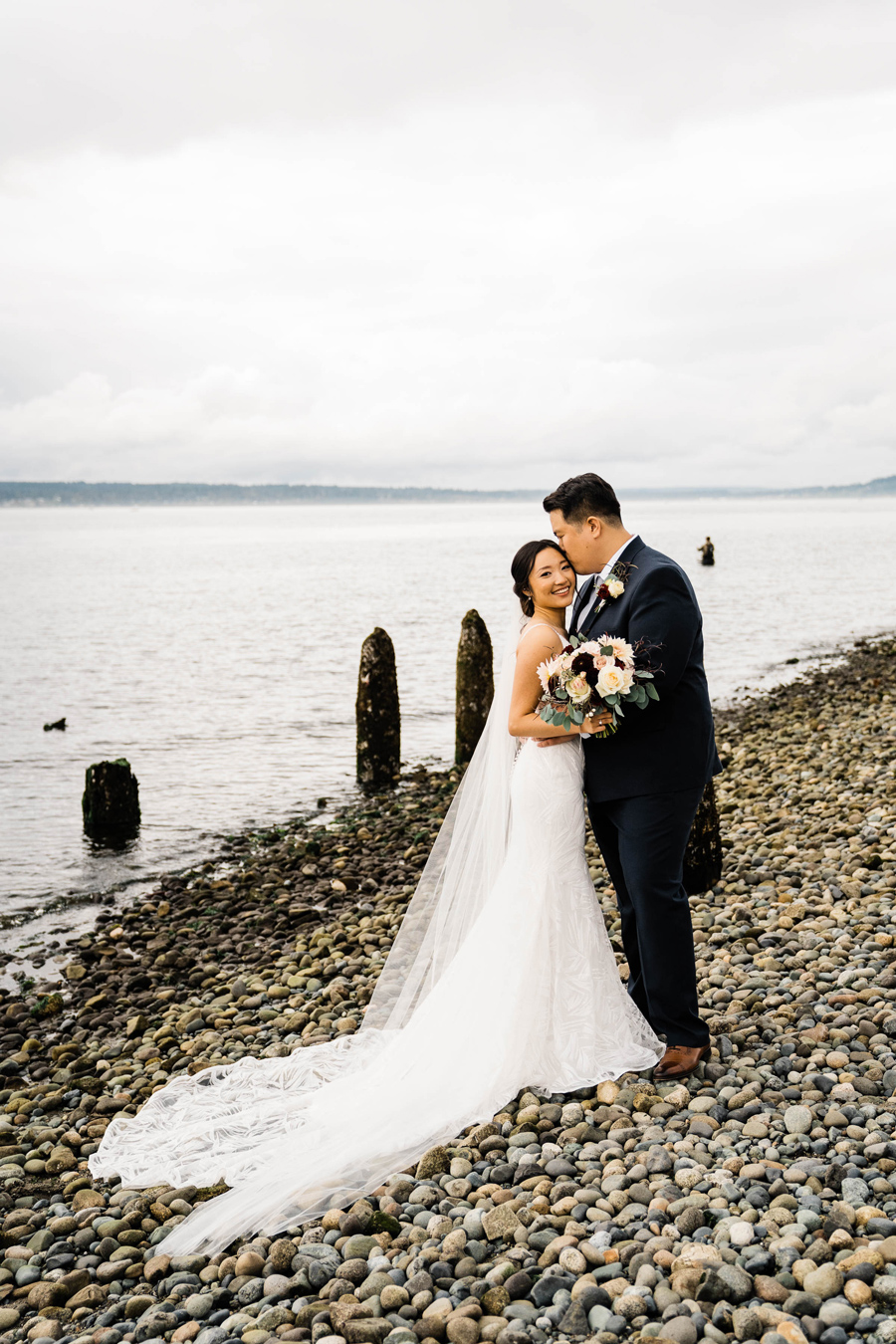 A bride and groom snuggle together on a beach on their wedding day near Seattle