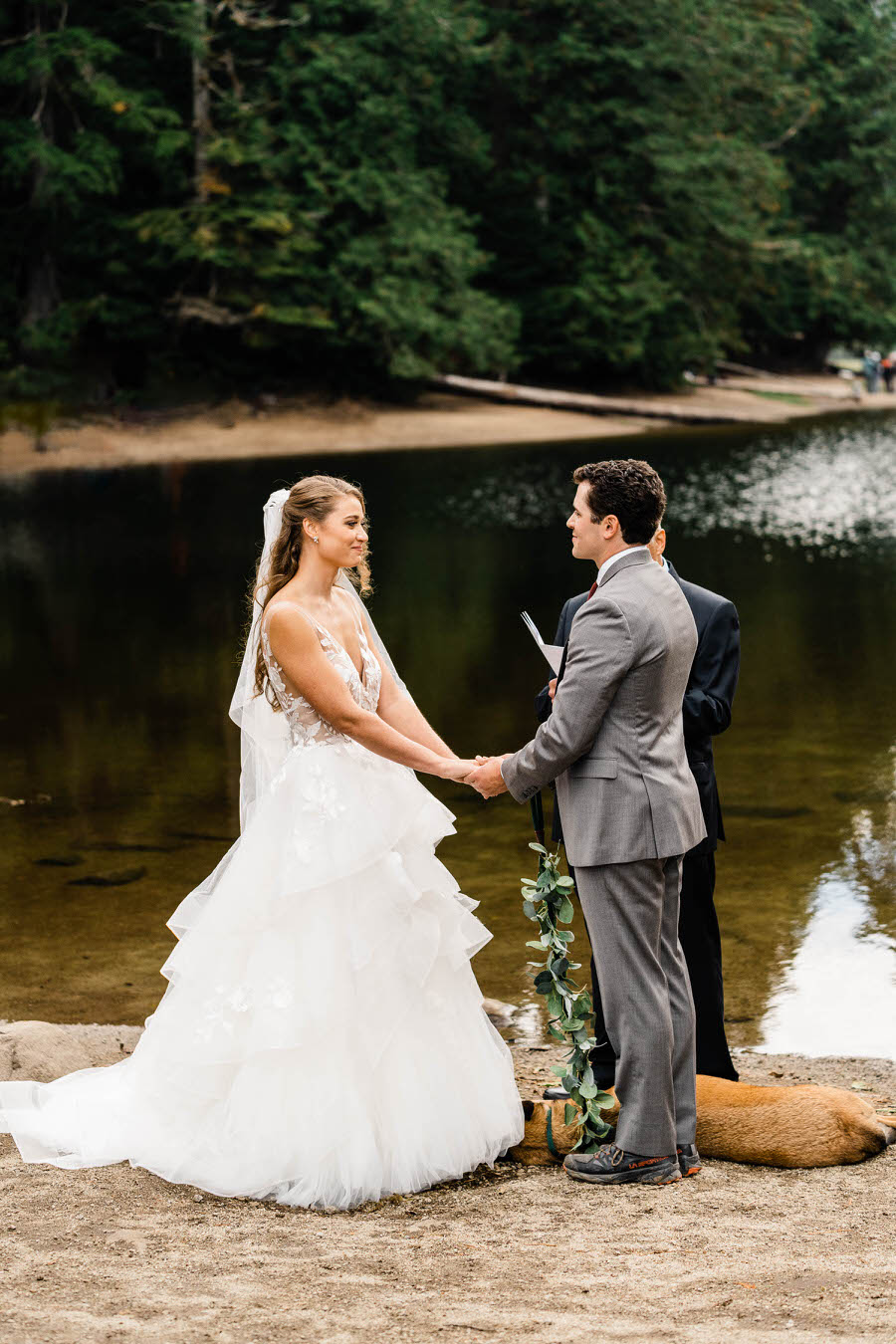 A bride and groom hold hands during their elopement ceremony next to an alpine lake