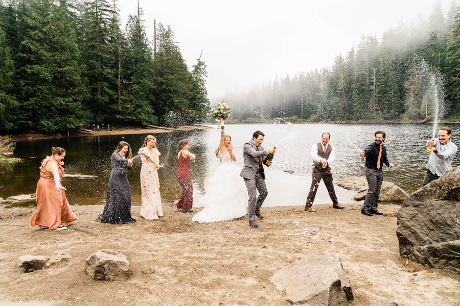 Champagne sprays everywhere after a hiking elopement ceremony next to an alpine lake