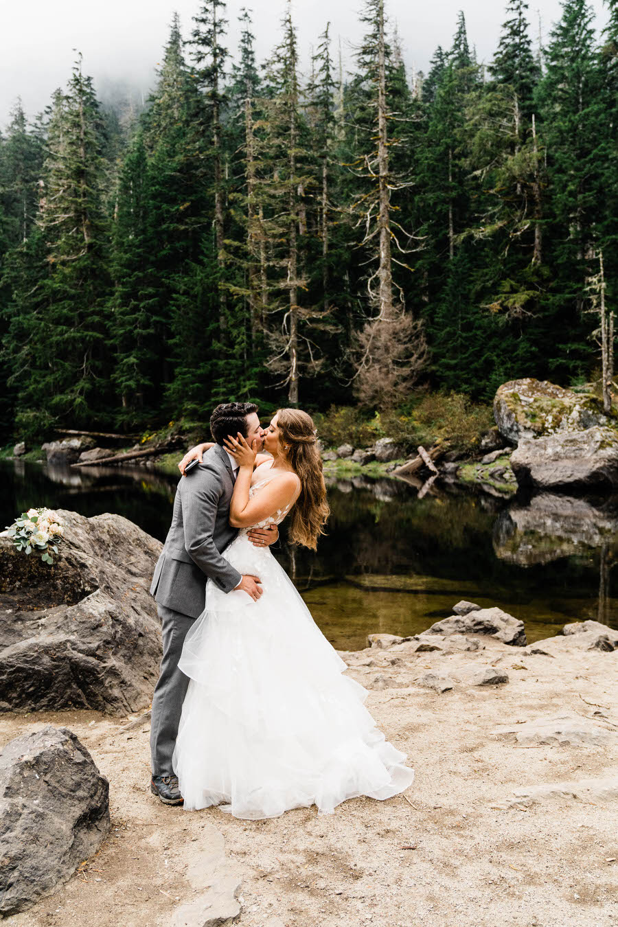 A bride and groom share a romantic kiss next to an alpine lake in the Washington backcountry