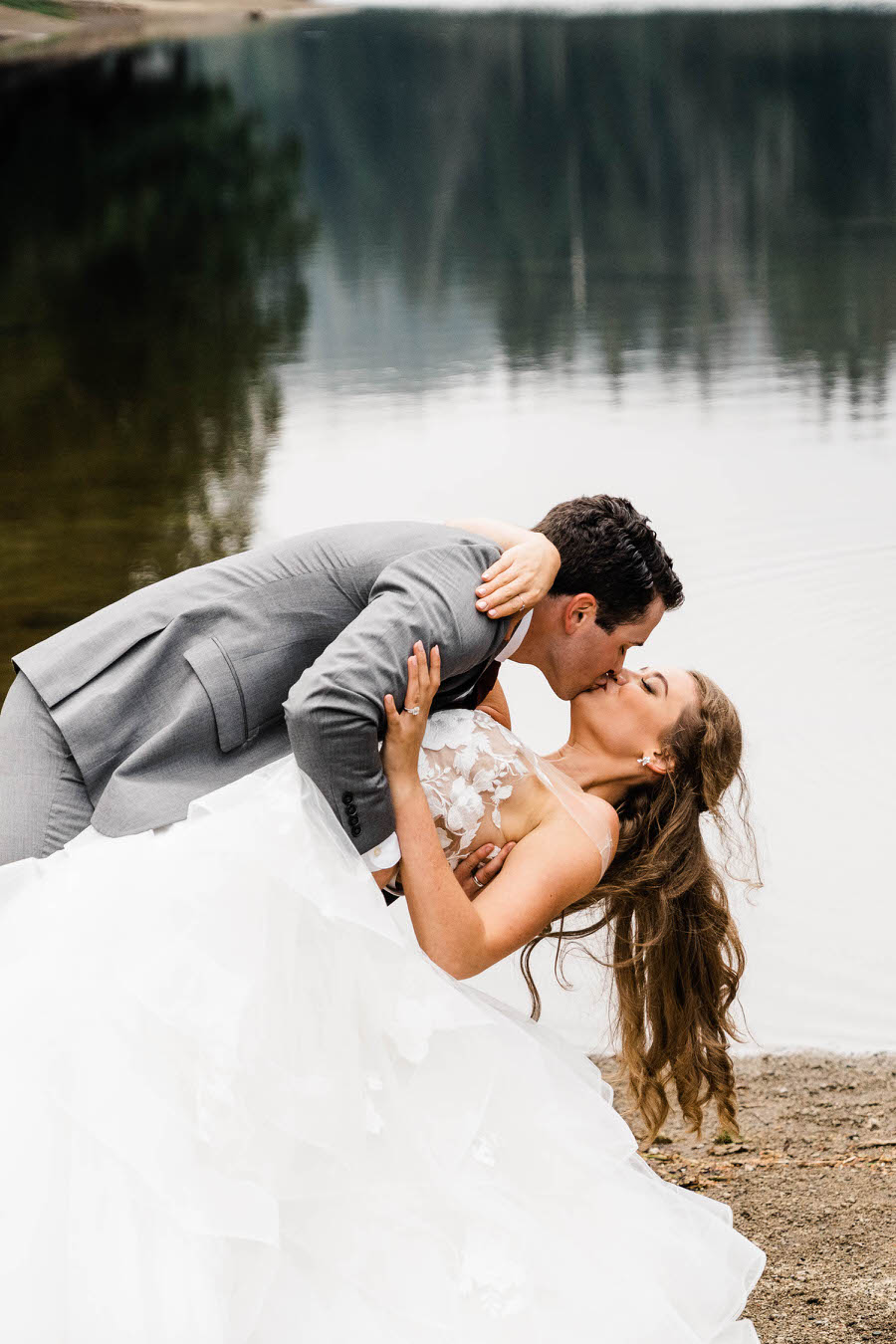 A groom dips his bride next to an alpine lake