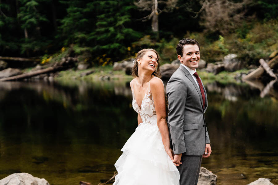 A bride and groom stand back-to-back and giggle together after their hiking elopement in Washington