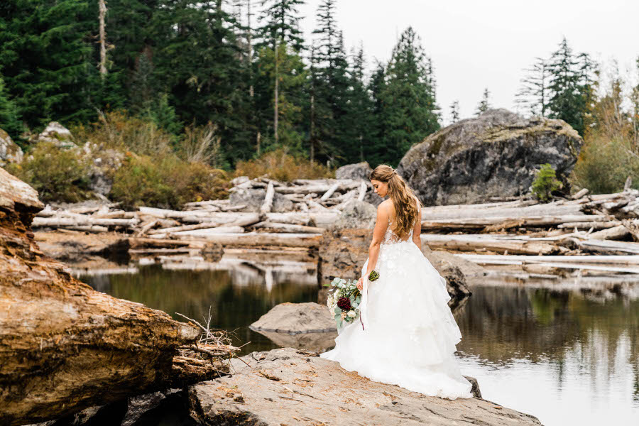 A bride wearing a layered wedding dress takes a moment to soak in the scenery after her hiking elopement in Washington