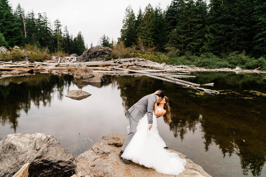A groom dips his bride next to a small pond in the Washington backcountry