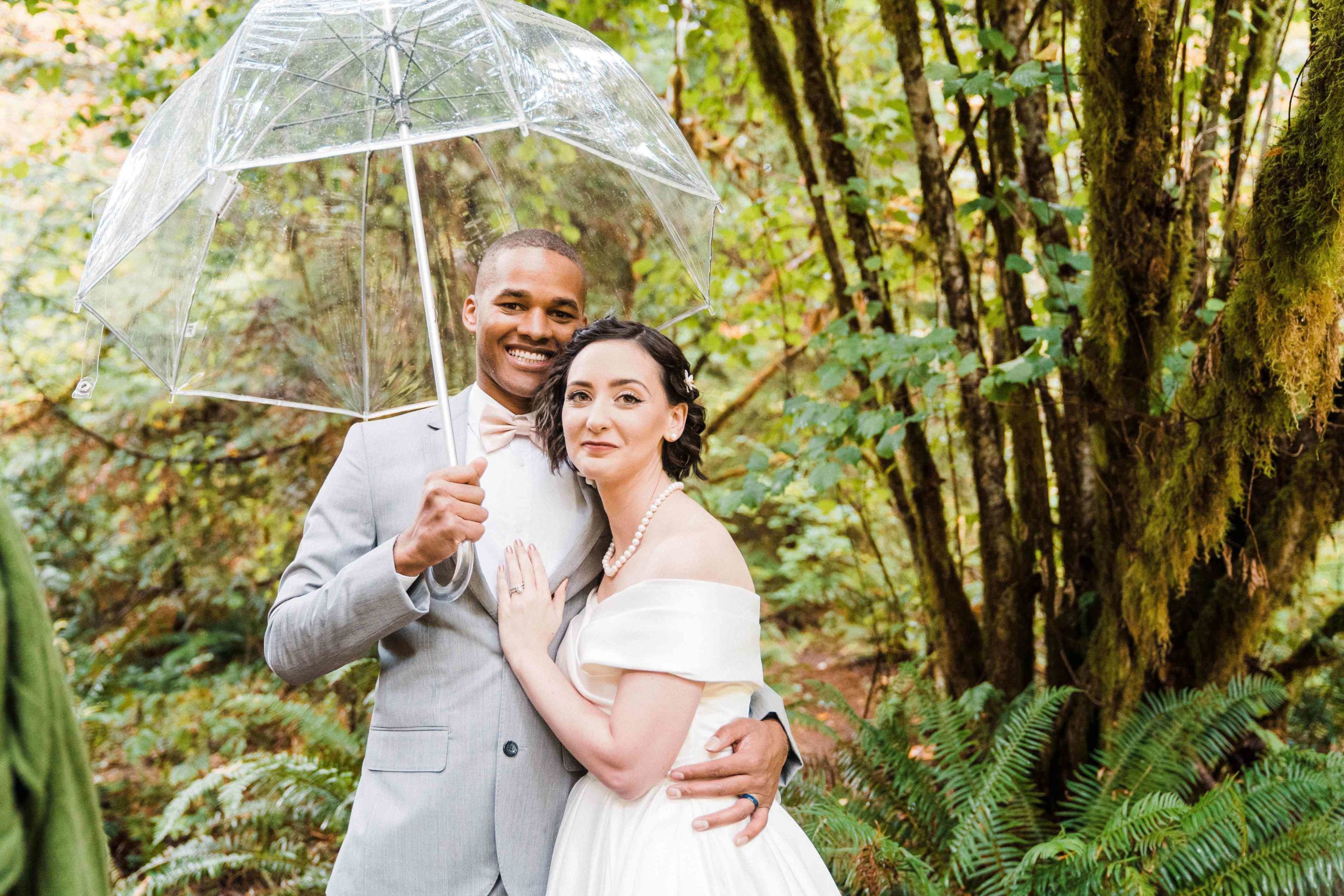 Bride and groom holding clear umbrella for couple portraits at Treehouse Point elopement
