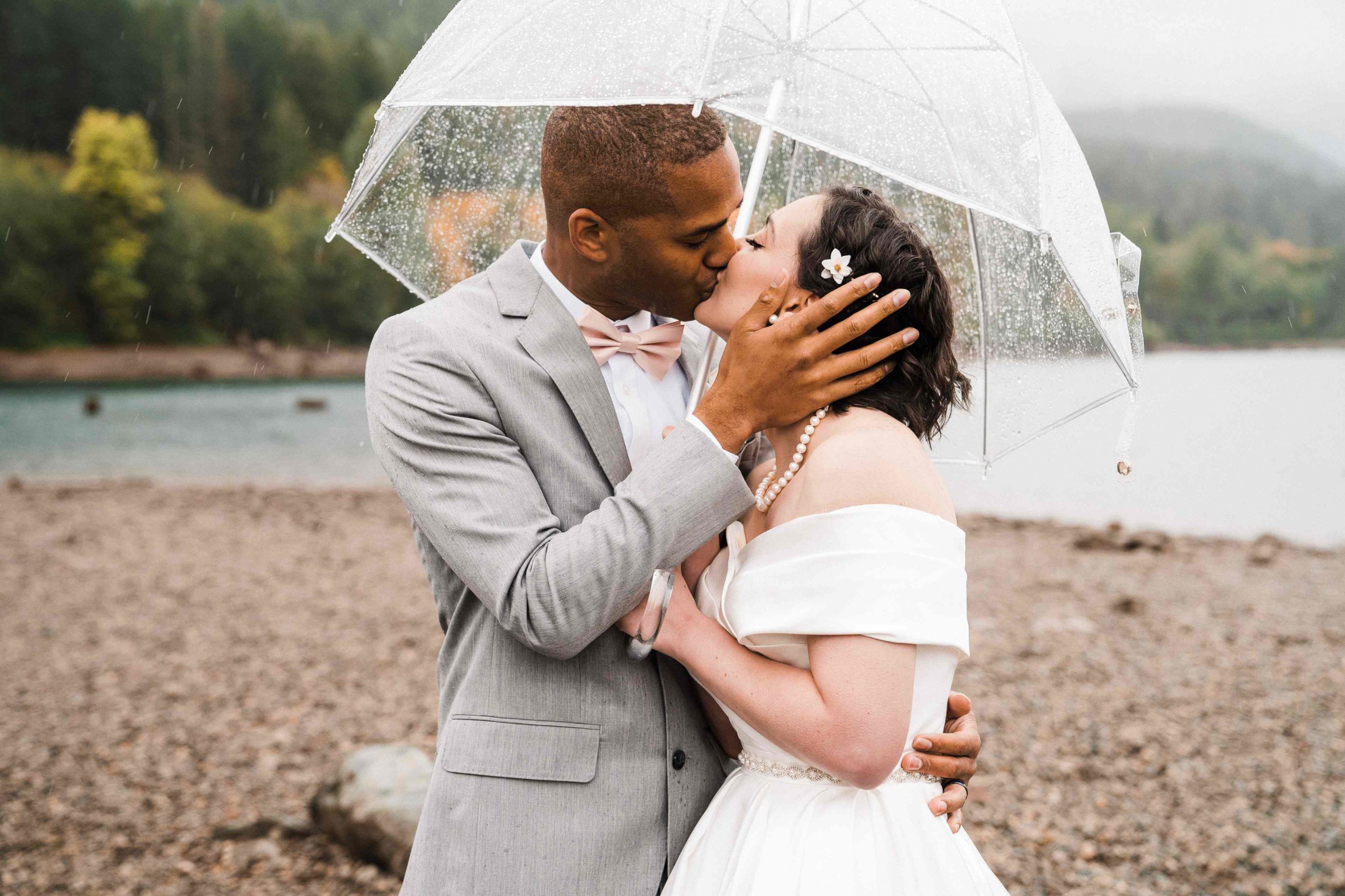 Bride and groom kiss under a clear umbrella at Rattlesnake Lake