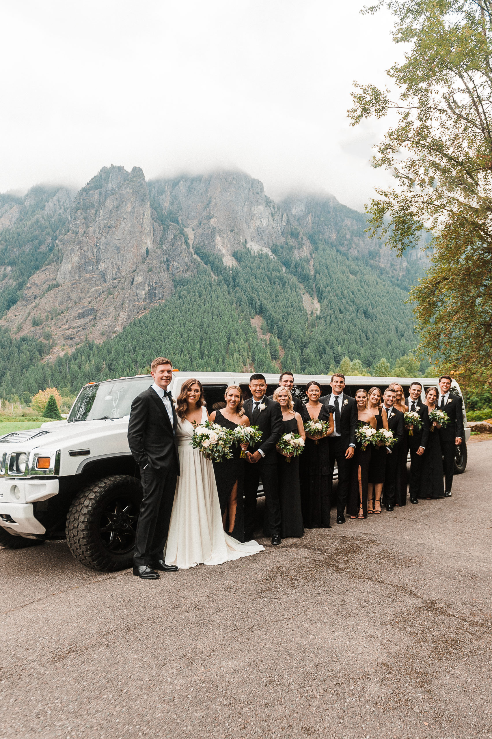Wedding party standing in front of white hummer limousine at the base of the PNW mountains