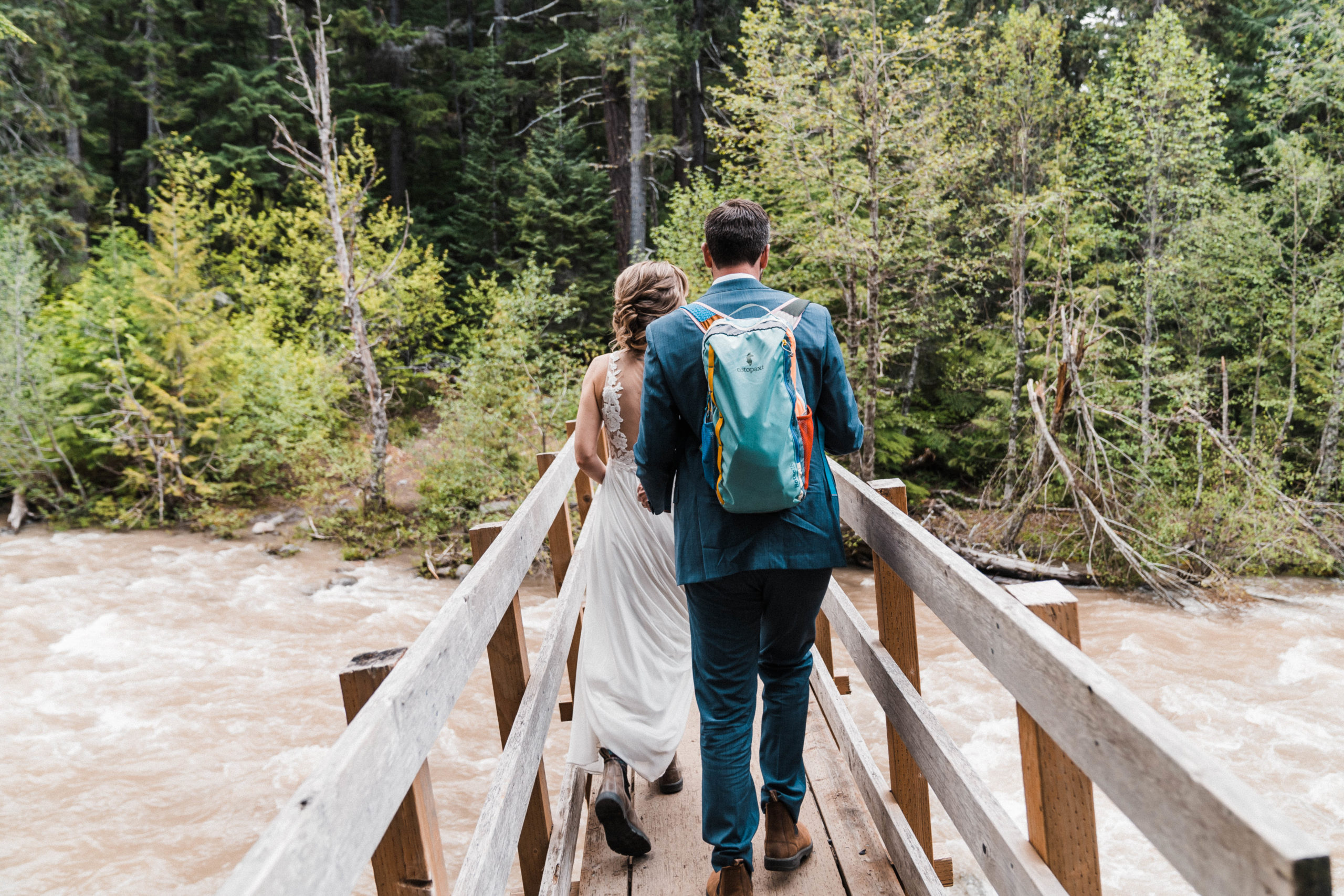 Bride and groom walking across wood bridge at hiking wedding in Hood River