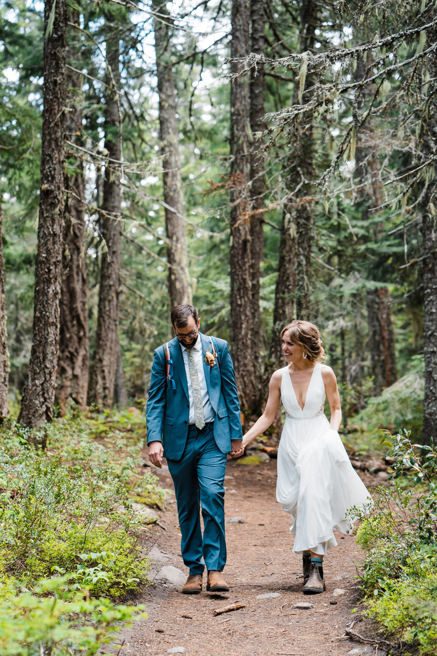 Bride and groom holding hands while walking through the forest at hiking wedding