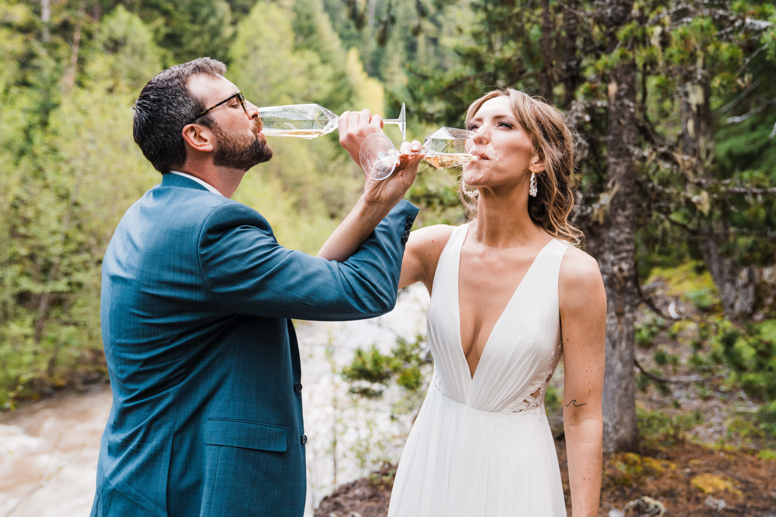 Bride and groom drinking champagne in the forest during hiking wedding