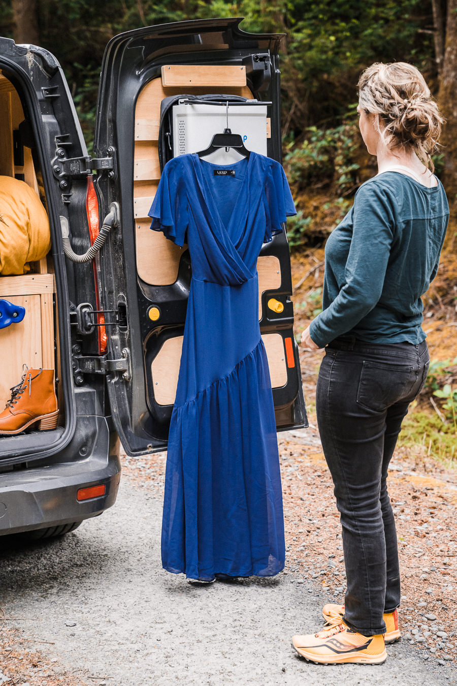 bride stands in front of her blue wedding dress hanging on her camper van