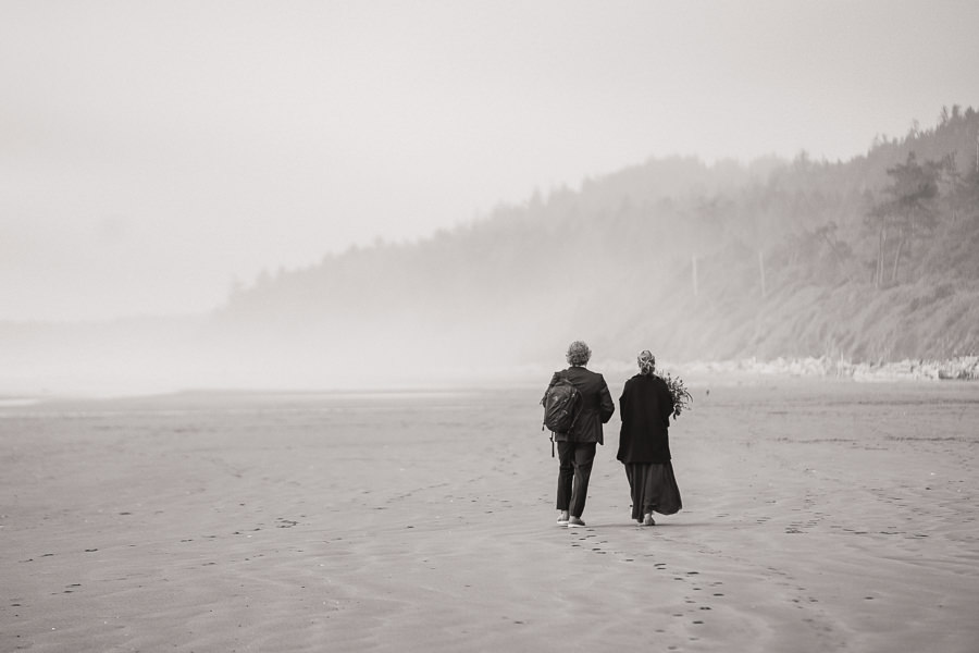 Black and white image of a bride and groom walking on a misty beach on the Washington coast