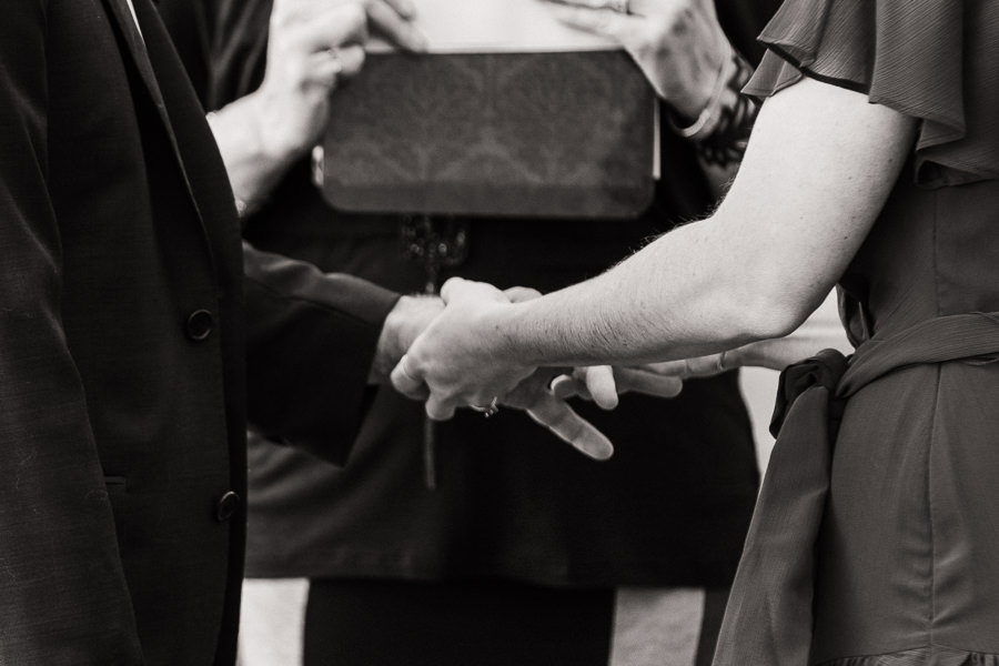 Black and white image of a bride putting a ring on her groom's finger