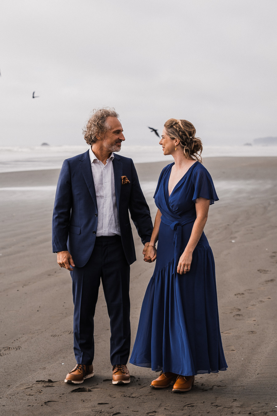 Bride and groom share a look after getting married on Kalaloch Beach as seagulls fly overhead