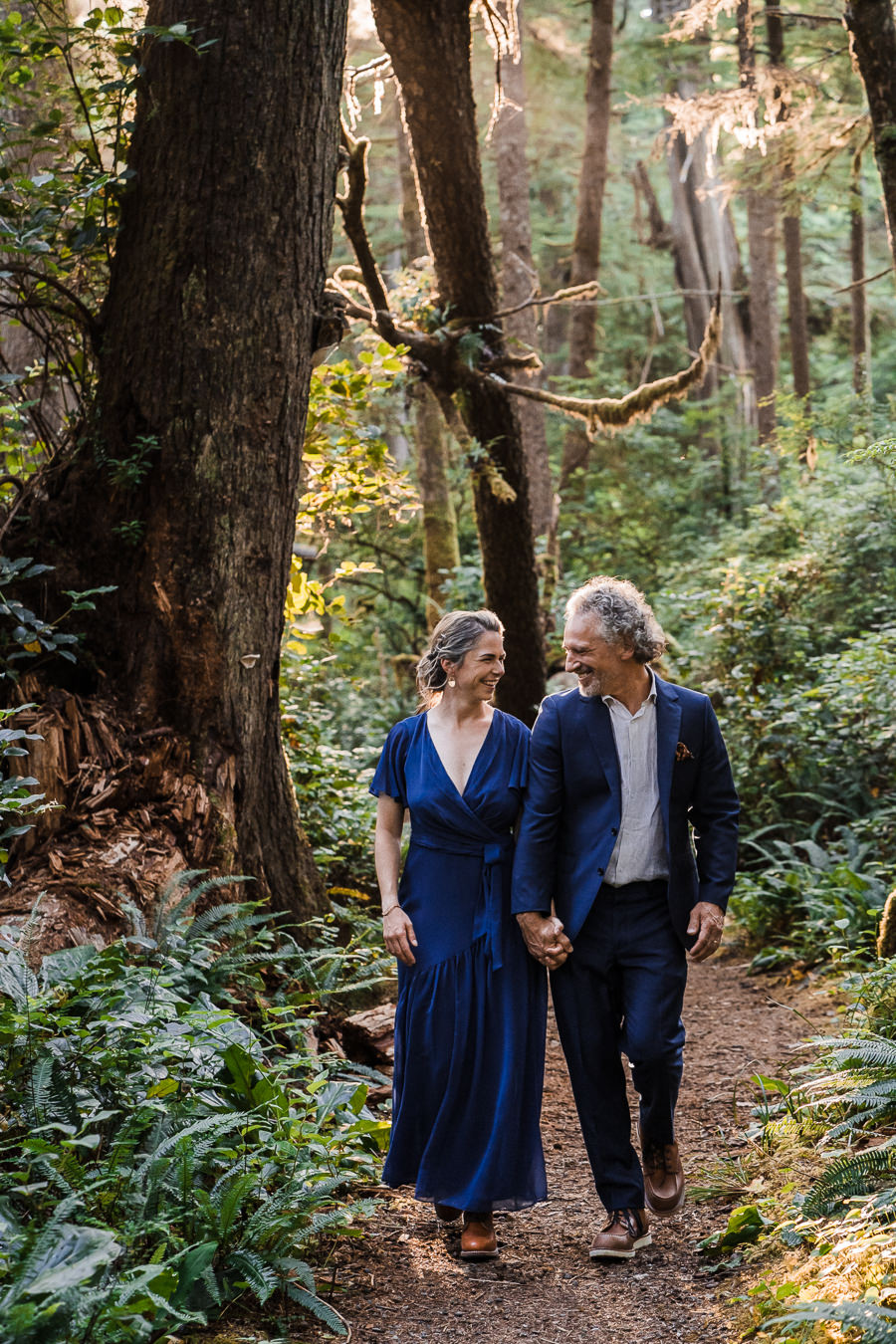 Bride and groom laugh and walk together in the mossy woods of Olympic National Park