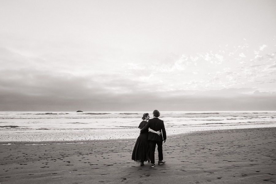 Black and white image of a bride and groom walking along Kalaloch Beach after their Washington coast elopement