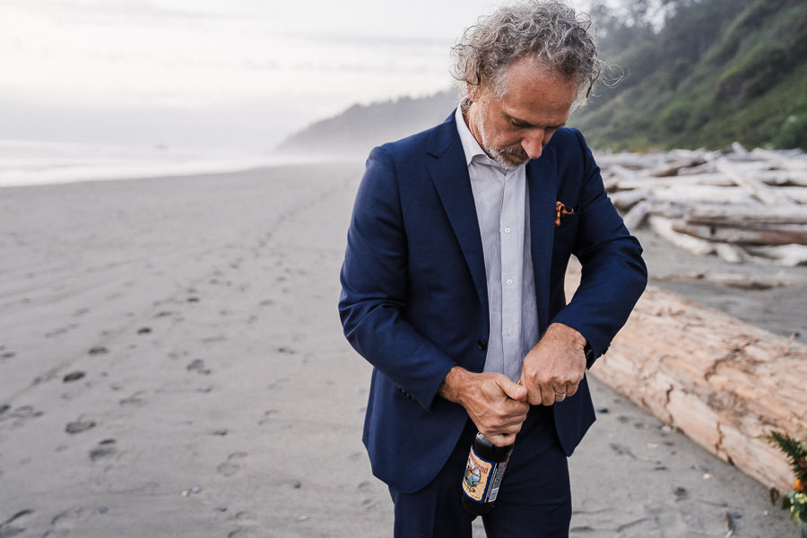 Groom opens a bottle of beer on the beach