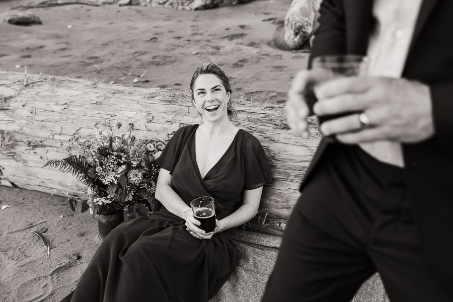 A bride gives her groom a smile while sitting next to driftwood