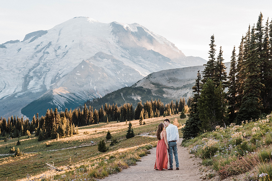 a couple walks down a trail with Mt Rainier in the background