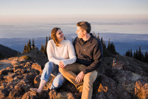 a couple sits on a rock together on top of a mountain in olympic national park