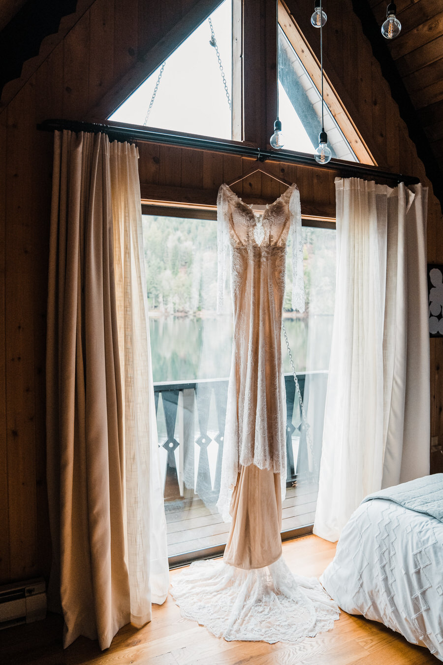 a long-sleeved wedding gown hanging from a beach in a lakefront cabin