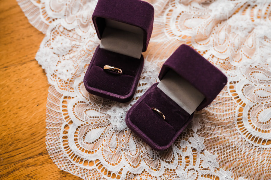 Gold wedding rings inside purple velvet boxes on top of white lace