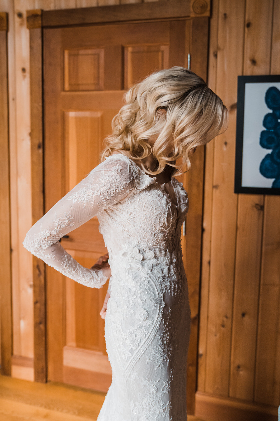 A bride zips up the back of her long-sleeved lace wedding gown